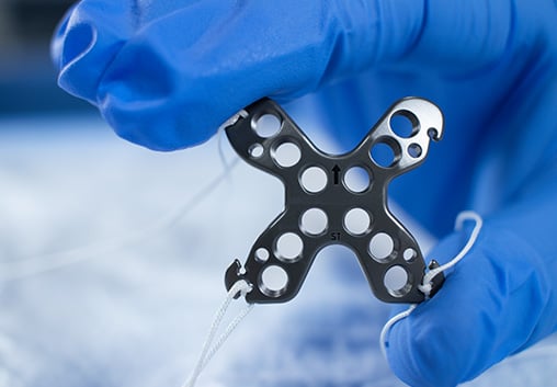 The Summit™ Patella Plate with attached sutures held in gloved fingers