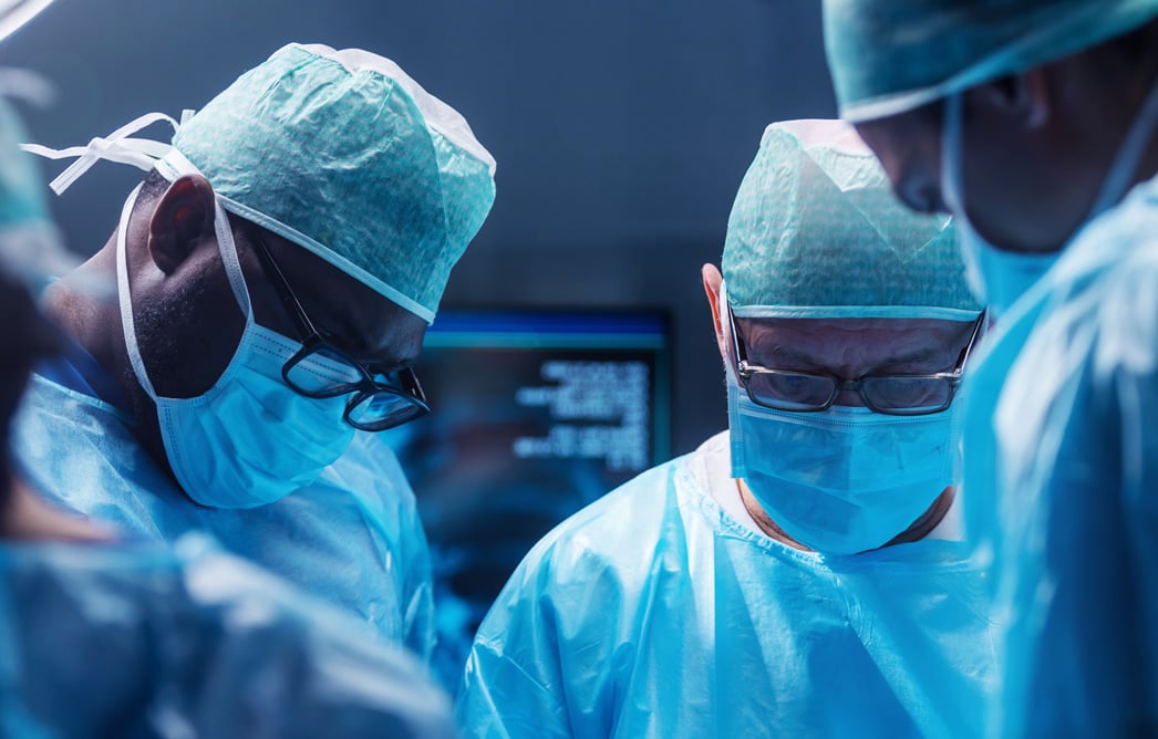 Surgical team in caps and masks working together over a patient