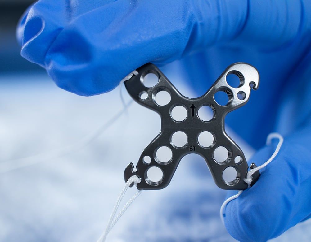 Gloved fingers holding The Summit™ Patella Plate