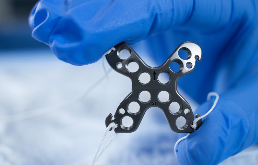Gloved fingers holding The Summit™ Patella Plate